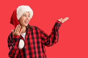 Pajamas Prints: Beautiful young woman in checkered pajamas and Santa hat on red background