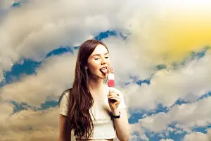 Licking Prints: Beautiful young woman licking popsicle against cloudy sky