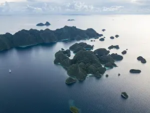 A bird's eye view shows dramatic limestone islands rising from the peaceful, tropical seascape in Raja Ampat, Indonesia