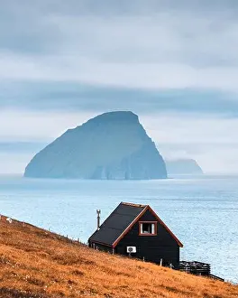 Black house on famous faroese Witches Finger Trail and Koltur island on background. Sandavagur village, Vagar island, Faroe islands, Denmark