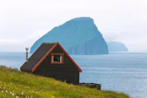Black house on famous faroese Witches Finger Trail and Koltur island on background. Sandavagur village, Vagar island, Faroe islands, Denmark