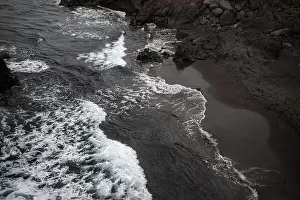 Black sand beach aerial view. Small volcanic rocks and graphic diagonal waves