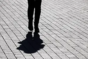 Unrecognizable Prints: Black silhouette and shadow of lonely woman walking on a street