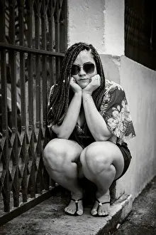 Braid Prints: Black and white portrait of a woman wearing sunglasses crouching down looking at the camera with her hands on her chin