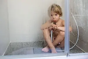 Blond child, sweet toddler boy in bathroom, taking shower, sitting on the floor, punished