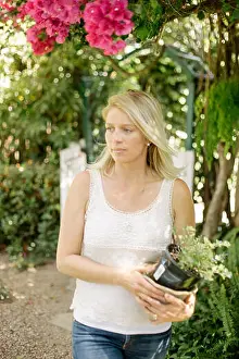 Mid Adult Women Prints: Blond woman in a garden, holding a plant pot