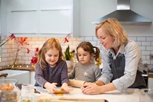 Freetime Prints: Blond woman wearing blue apron and two girls standing in kitchen, baking Christmas cookies