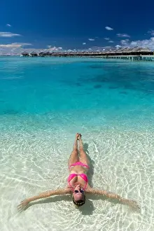 Beachfront Prints: Blonde caucasian woman wearing pink bikini laying down in water at Anantara Dhigu and Vela luxury hotel Maldives