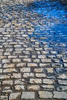 Puddle Prints: Blue spring sky reflected in the puddles on the cobblestone pavement close-up