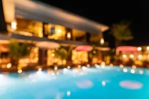 Blur lights reflection in infinity swimming luxury pool party water at night background. Resort hotel abstract bokeh background summer travel vacation