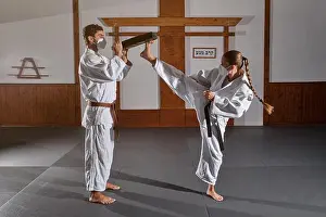 Concentrate Prints: Full body of male and female wearing kimono and medical masks doing Krav Maga kicks in modern room