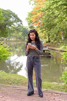 Texting Prints: Full body shot of young beautiful Indian woman using phone at the park outdoors