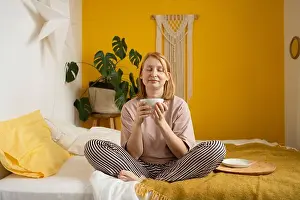 Awake Prints: Full body of smiling ginger barefoot lady in striped pants sitting on comfortable bed