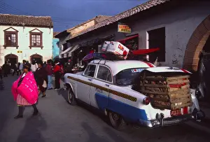 Bolivia Prints: Bolivia Potosi street scene Woman wearing tradition pink shawl and huge american car with full boot