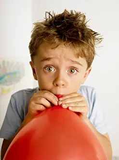 Eyed Prints: boy 7 blowing up a red balloon for a birthday party looking wide eyed
