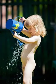 boy pouring water on himself from watering-can during hot summer