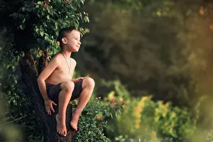 Throw Prints: A boy without a shirt sits on a partially felled tree in the village