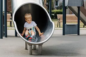 Playtime Prints: A boy slides down a metal enclosed circular tunnel slide