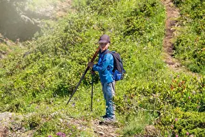 Caucasus Prints: A boy traveler with trekking poles is standing on the path to the top of the mountain range