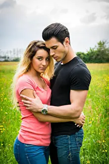 Cuddling Prints: Boyfriend and girlfriend standing in countryside in green luscious field