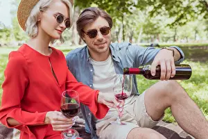 Red Dress Prints: boyfriend pouring red wine in glasses from bottle in park