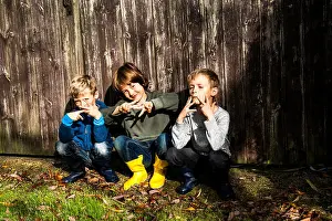 Three boys, outdoors, crouching beside fence, making hand gestures
