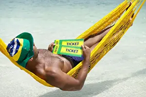 2014 Prints: Brazilian man relaxing in beach hammock with two Brazil tickets