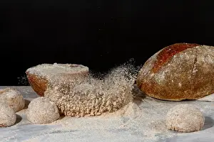 Scattered Prints: A bread loaf splash on a pile of wholewheat flour on marble countertop with dark background