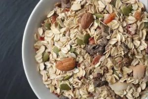 Porridge Prints: Breakfast oat muesli with nuts, seeds and dried fruits in a white bowl on dark background