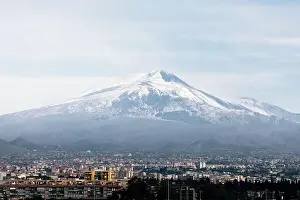 Breathtaking drone view of Mont Etna with snowy peak located near Catania city on cloudy day in Sicily, Italy