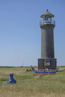 Grass Field Prints: Brick lighthouse next to boat and blue sculpture in a meadow under blue sky