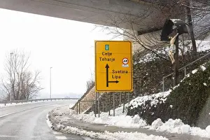 Snowfall Prints: Bright yellow road sign under an overpass directs travelers to Celje