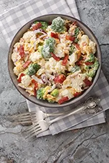 Broccoli cauliflower bacon bound salad with cheese mayonnaise dressing closeup on the plate on the table. Vertical top view from above