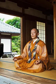 Eyes Closed Prints: Buddhist monk with shaved head wearing golden robe sitting cross legged on the floor