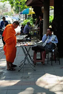 Chiang Mai Prints: Buddhist monk wearing an orange robe and buying a watch in a street of Chiang Mai