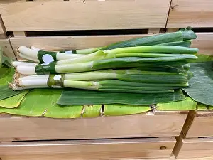 Stalk Prints: Bunches of fresh Japanese bunching onions or Negi wrapped in banana leaf displayed on a wooden crate in a supermarket