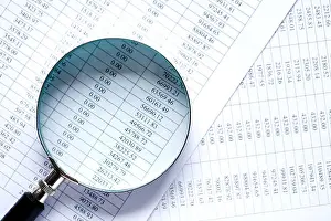 Searching Prints: Business research. Closeup of magnifying glass on paper with digits