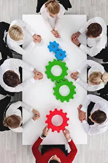 Colleagues Prints: Business team sitting around the table with cogs, teamwork concept