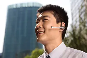 On The Move Prints: Businessman on Bluetooth phone in front of skyscraper