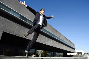 Office Building Prints: Businessman wearing blue suit and tie jumping with open arms in urban background