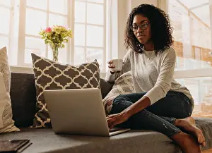 Curly Hair Prints: Businesswoman working on laptop computer sitting at home holding a coffee cup in hand