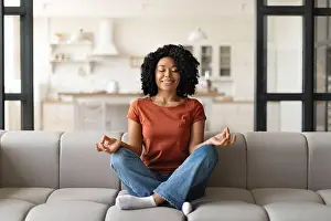 Practicing Prints: Calm black woman sitting on couch, meditating with closed eyes at home