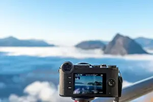 Lugano Prints: Camera Filming Mountain Peak San Salvatore Above Cloudscape with Sunlight and Clear Sky in Lugano