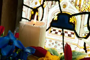 A candle burning in front of a stained glass window in a church