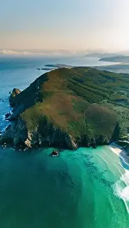 Captivating drone shot capturing the serene beauty of a green peninsula surrounded by turquoise waters in Galicia