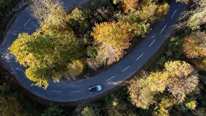 Car driving on a mountain road surrounded by fall season forest. Aerial photography