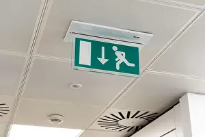 Fire Escape Prints: Ceiling mounted LED emergency fire exit sign with arrow pointing towards the fire door in a UK office