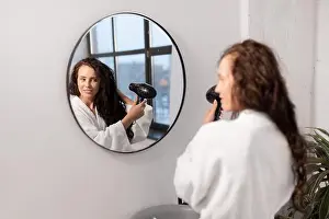 Only Women Prints: Charming young female with hair-dryer taking care of her dark long wavy hair
