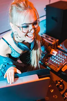 Nightclub Prints: cheerful blonde dj girl in headphones using laptop in nightclub