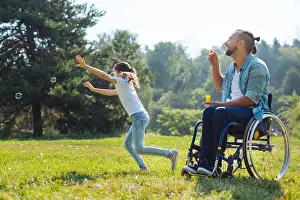 Paralysis Prints: Cheerful disabled father and daughter playing with soap bubbles